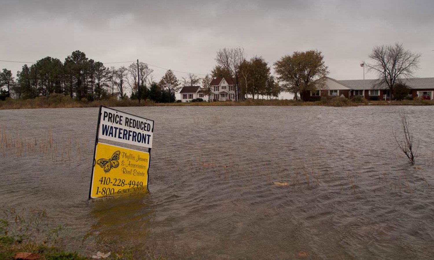 A waterfront property for sale sign submerged in flood waters