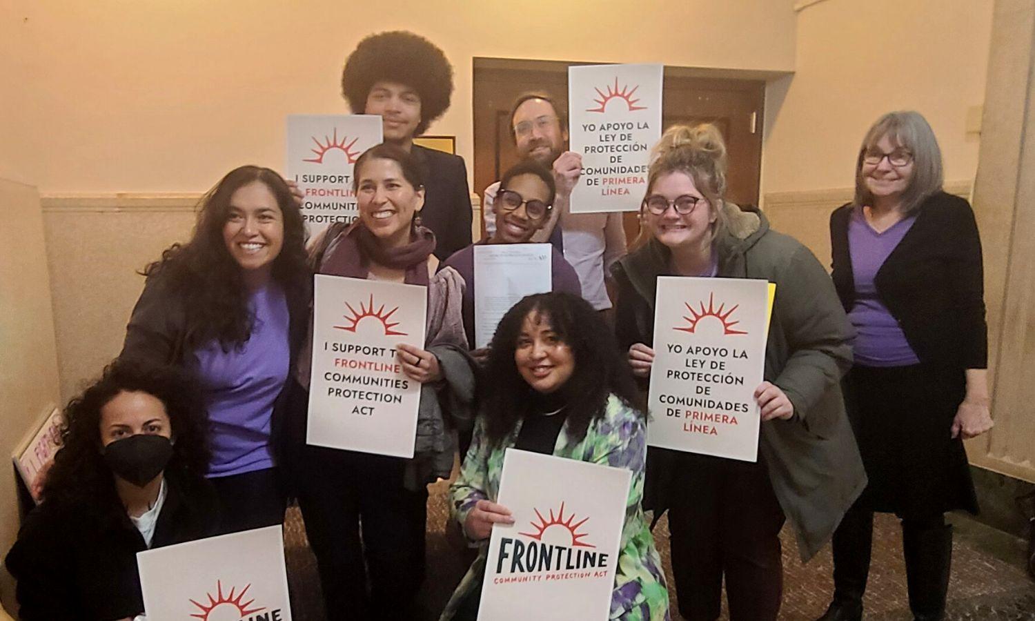 A group of people hold signs showing support for frontline communities.