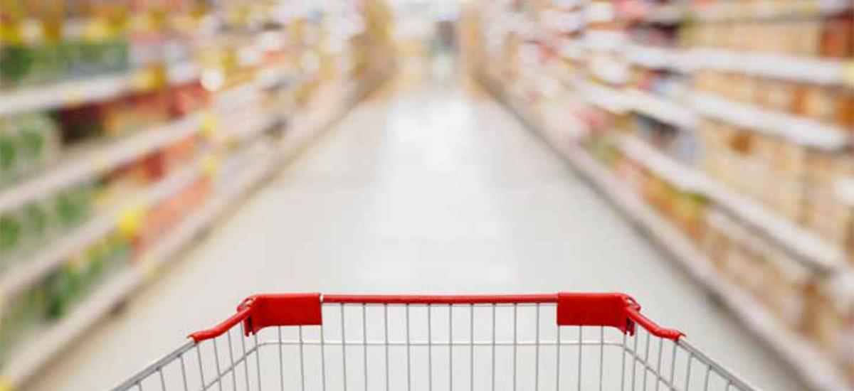 Shopper's-eye view of a shopping cart in a supermarket aisle.