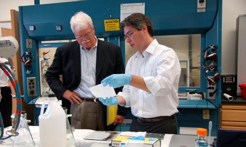 Scientist giving demonstration to legislator in lab.