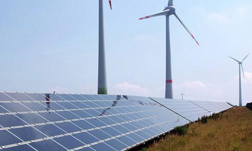 Solar panels in a field with three wind turbines behind them