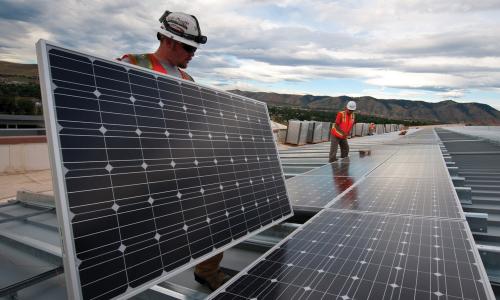 Two workers with hardhats installing rooftop solar panels