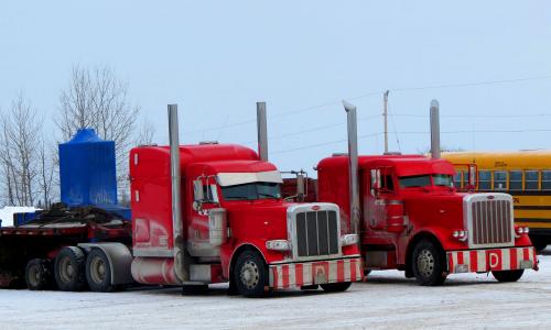 Two red trucks in parking lot next to school bus