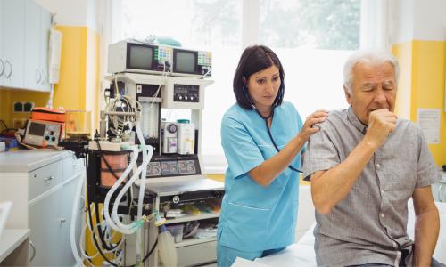 An older man coughing in a hospital bed