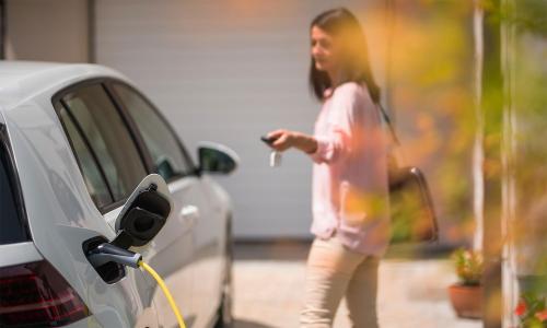 Woman using key fob to lock white electric vehicle that is charging