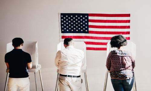 Three people hunched over behind privacy screens, voting.