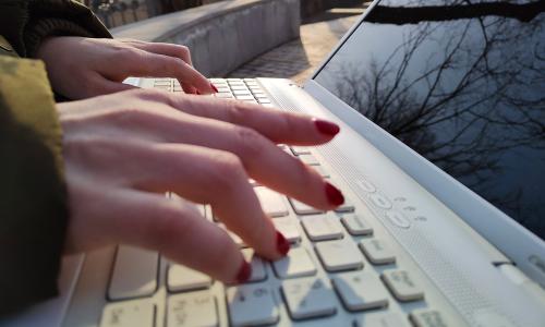 A person typing outdoors on a laptop.