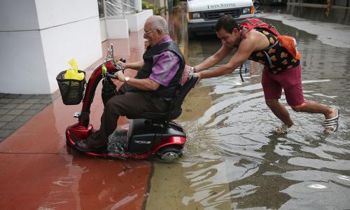 One man pushes another in a wheelchair through Miami floodwaters