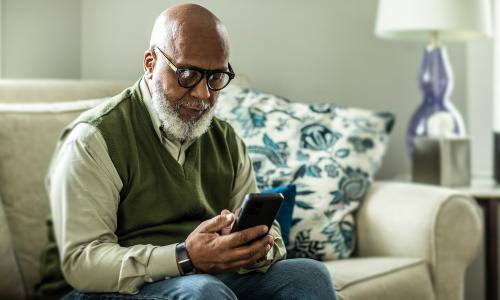 A senior man sitting on a couch using a smartphone.