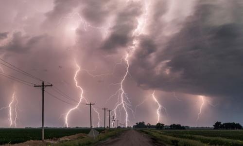 A photo of power lines along a road with lightning striking in the distance.