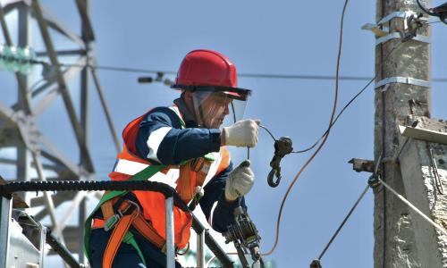 a linesman with red helmet and orange safety vest works on a powerline