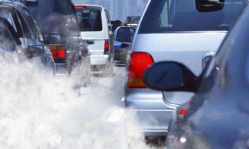 Cars in traffic sitting in a cloud of exhaust smoke.